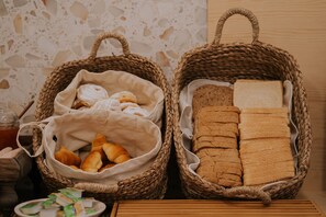 Two woven baskets containing bread and pastries, with a tiled wall in the background.