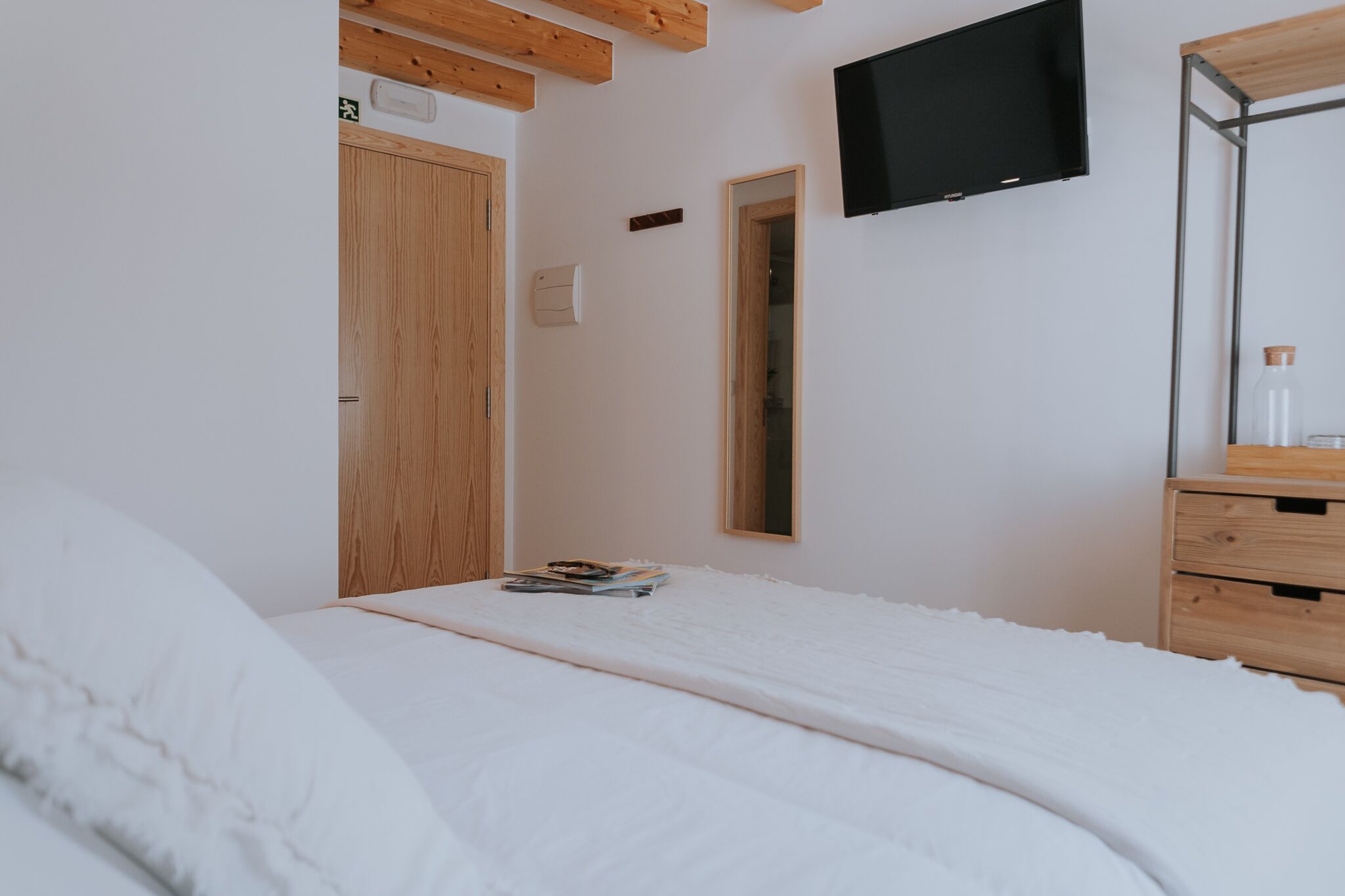 A bedroom with a bed, wooden headboard, a flat-screen TV mounted on the wall, a wooden dresser, and a mirror.