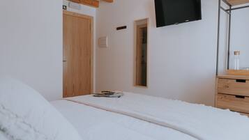 A bedroom with a bed, wooden headboard, a flat-screen TV mounted on the wall, a wooden dresser, and a mirror.
