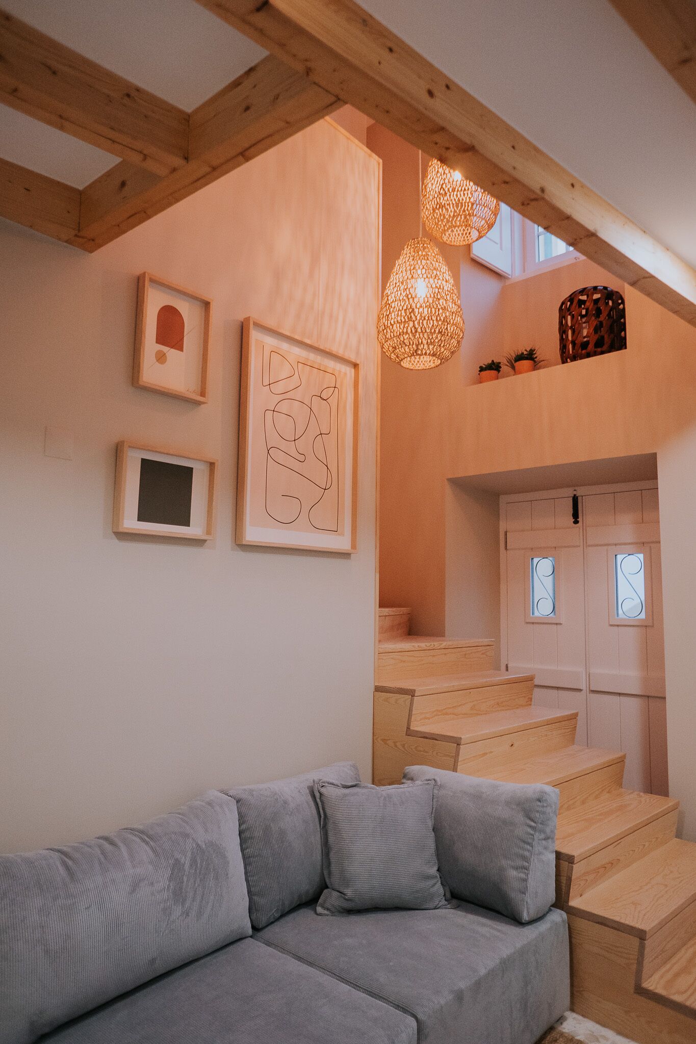 A modern interior with a grey sofa, wooden staircase, and framed artwork on the wall.