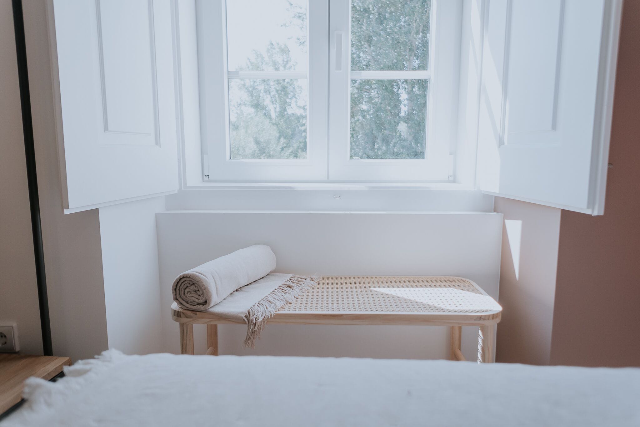 Une pièce avec un lit, un banc sur lequel est pliée une serviette, une fenêtre et une vue sur les arbres.