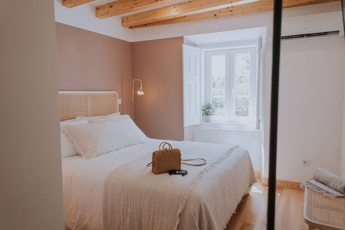 A bedroom with a bed, a bedside lamp, a window, and a chair.