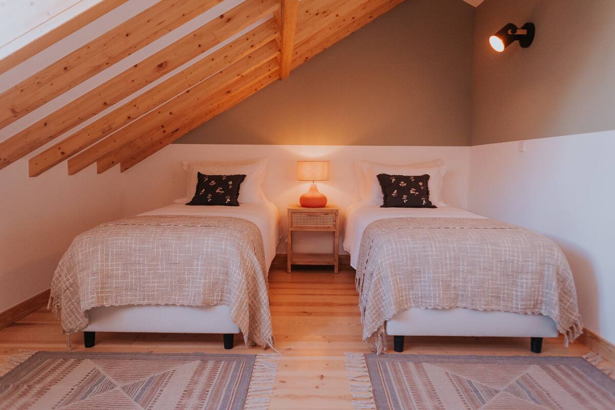 A bedroom with two beds, a nightstand, a lamp, and a wooden ceiling.