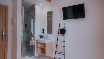 A modern bathroom with a glass shower, a white sink, a wooden vanity, a towel rack, and a mounted TV.
