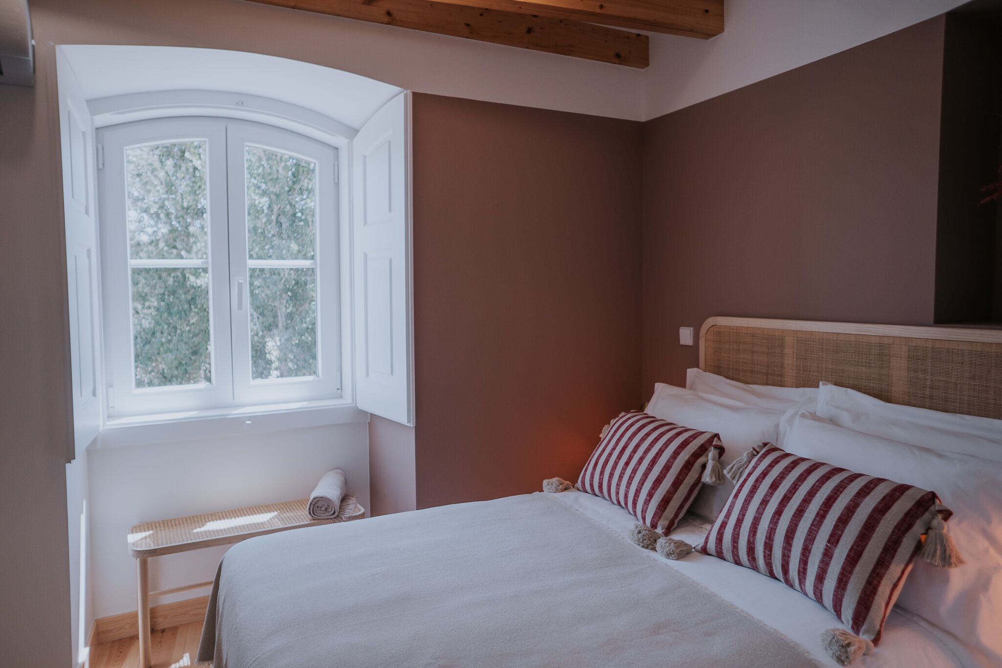 A bedroom with a large bed, a window with white shutters, and a wooden headboard.