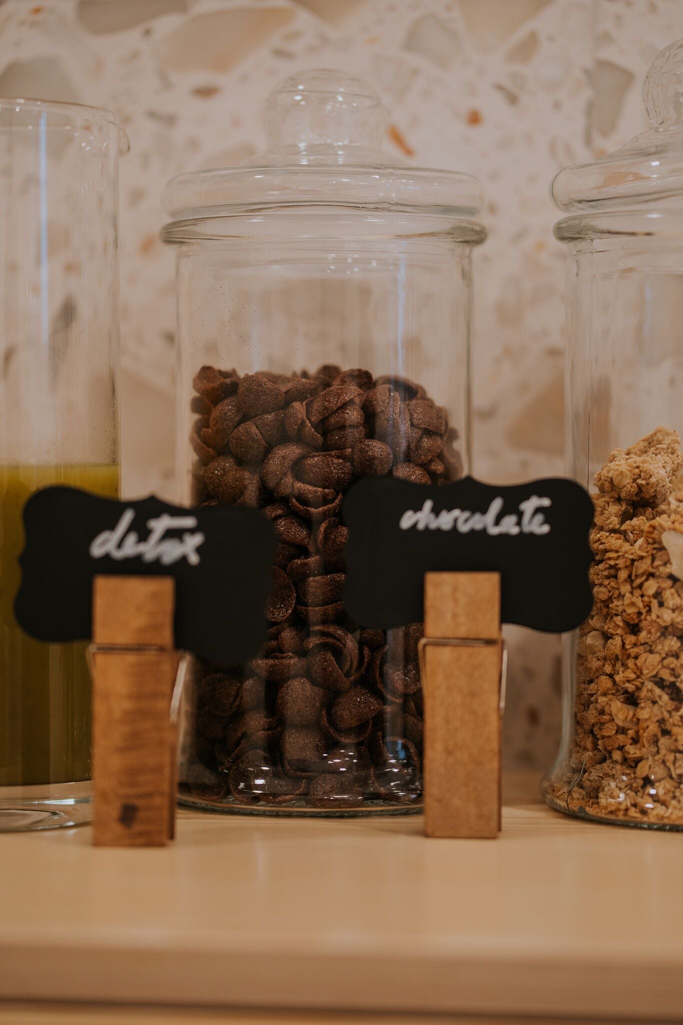 Three glass jars labeled "detox," "chocolate," and "granola" on a shelf.