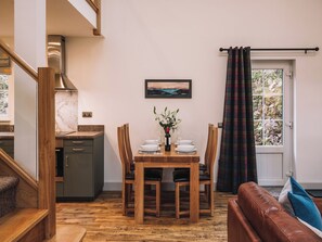 Ein Essbereich mit einem Holztisch und -stühlen, einem Bild an der Wand und Blick durch ein mit Vorhängen drapiertes Fenster.