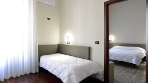 A hotel room with a single bed, a bedside table, a mirror, and a window with curtains. - Hotel Roma 62 (Palermo)