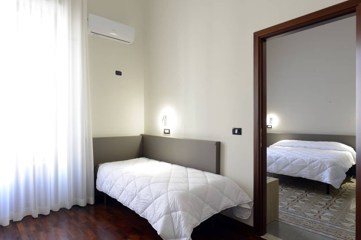 A hotel room with a single bed, a bedside table, a mirror, and a window with curtains.