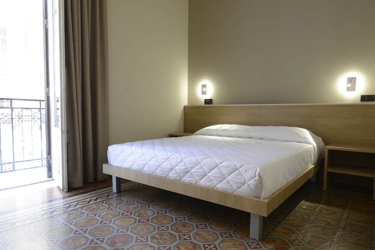 A hotel room with a bed, a nightstand, a wall-mounted light, and a patterned floor.