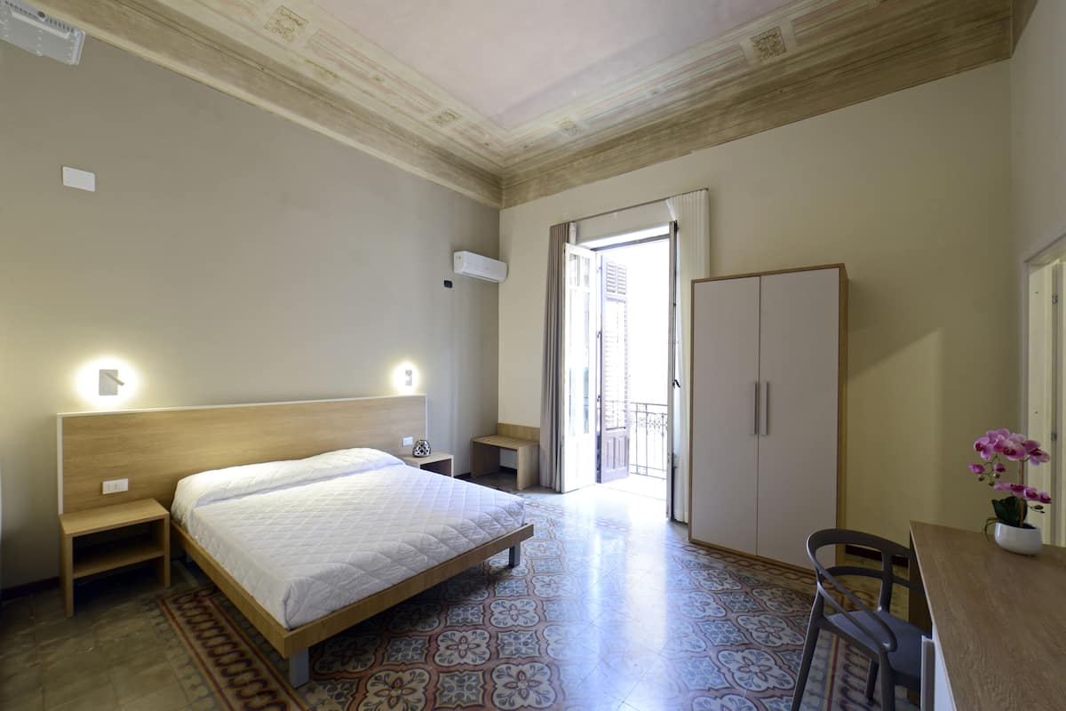 A bedroom with a bed, bedside table, wardrobe, and a view to the outside.