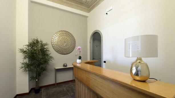A reception area with a wooden reception desk, a potted plant, a decorative wall piece, and a lamp. - Hotel Roma 62 (Palermo)