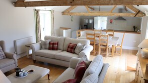 A cozy living room with a sofa, armchair, and a dining area with a table and chairs. A kitchen is visible in the background. - Clayhanger Lodge  - Abbotsbury, Dorset (Abbotsbury)