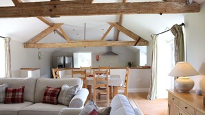A cozy living room with a sofa and chairs, wooden beams on the ceiling, a dining table with chairs, and a kitchen in the background. - Clayhanger Lodge  - Abbotsbury, Dorset (Abbotsbury)