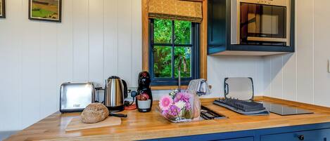 A kitchen with a wooden countertop, a toaster, a kettle, a coffee maker, a sink, and a window with a view of greenery.