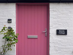 A pink door with a mailbox and a 'Bonnie Cottage' sign on a white brick wall. - Bonnie Cottage - UK40057 (Aberfeldy, near Pitlochry)