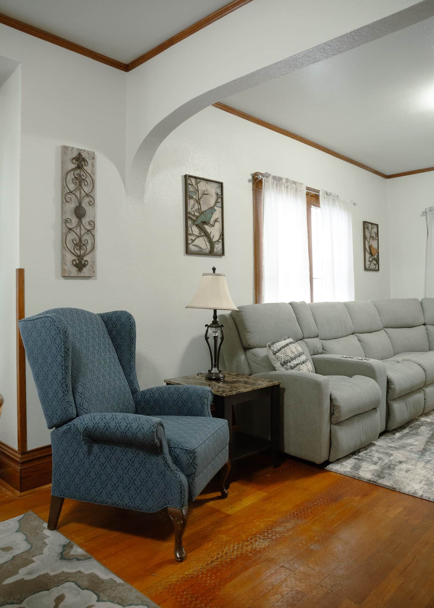 A living room with a blue armchair, a grey sofa, a lamp, and artwork on the walls.