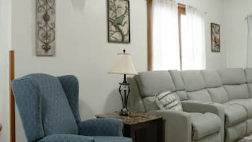 A living room with a blue armchair, a grey sofa, a lamp, and artwork on the walls.