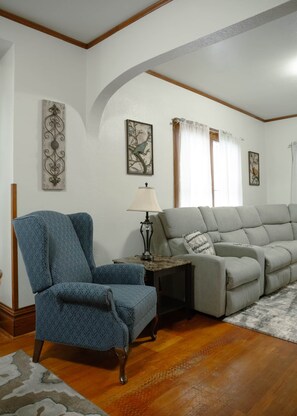 A living room with a blue armchair, a grey sofa, a lamp, and artwork on the walls. - Oahe Oasis – Spacious 4BR Mobridge Home (Mobridge)