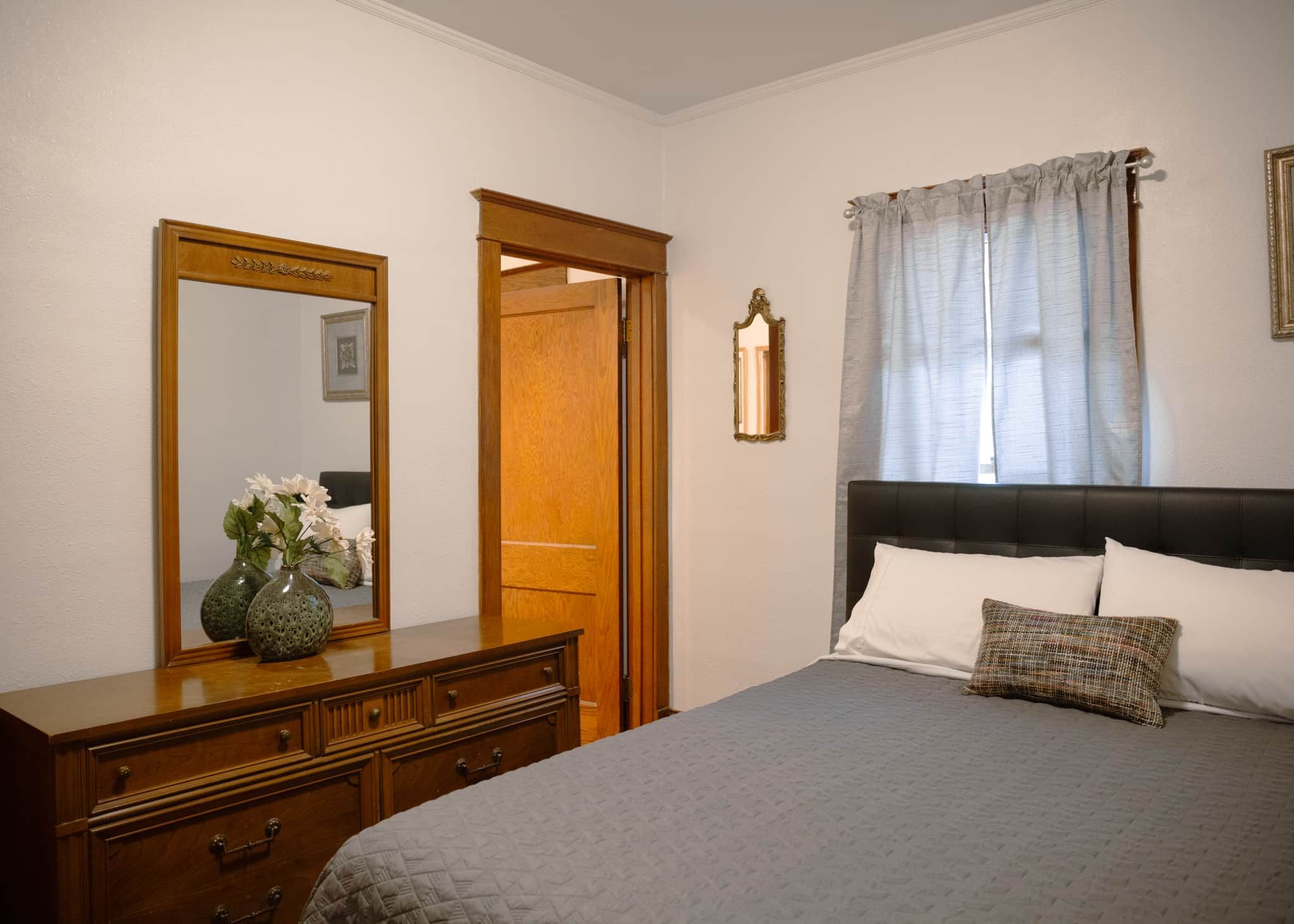 Un dormitorio con una cama, un aparador, un espejo y una puerta.