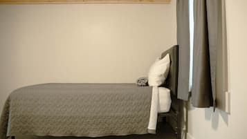 A single bed with a headboard, a pillow, and a blanket in a room with a wooden ceiling and a plain wall.