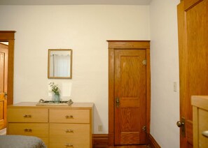A bedroom with a wooden dresser, a door, and a wall-mounted mirror.