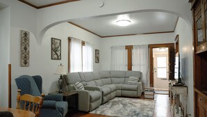 A living room with a sectional sofa, a wooden dining table, and a television.