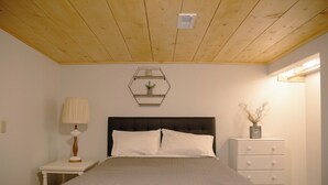 A bedroom with a bed, a nightstand, a dresser, and a wall-mounted shelf with a plant.