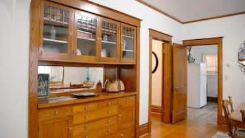 A wooden kitchen with a built-in cabinet, a dining area with a table and chairs, and a refrigerator in the background.