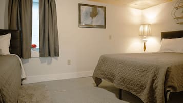 A room with two beds, a window with curtains, a wall-mounted lamp, and a painting.