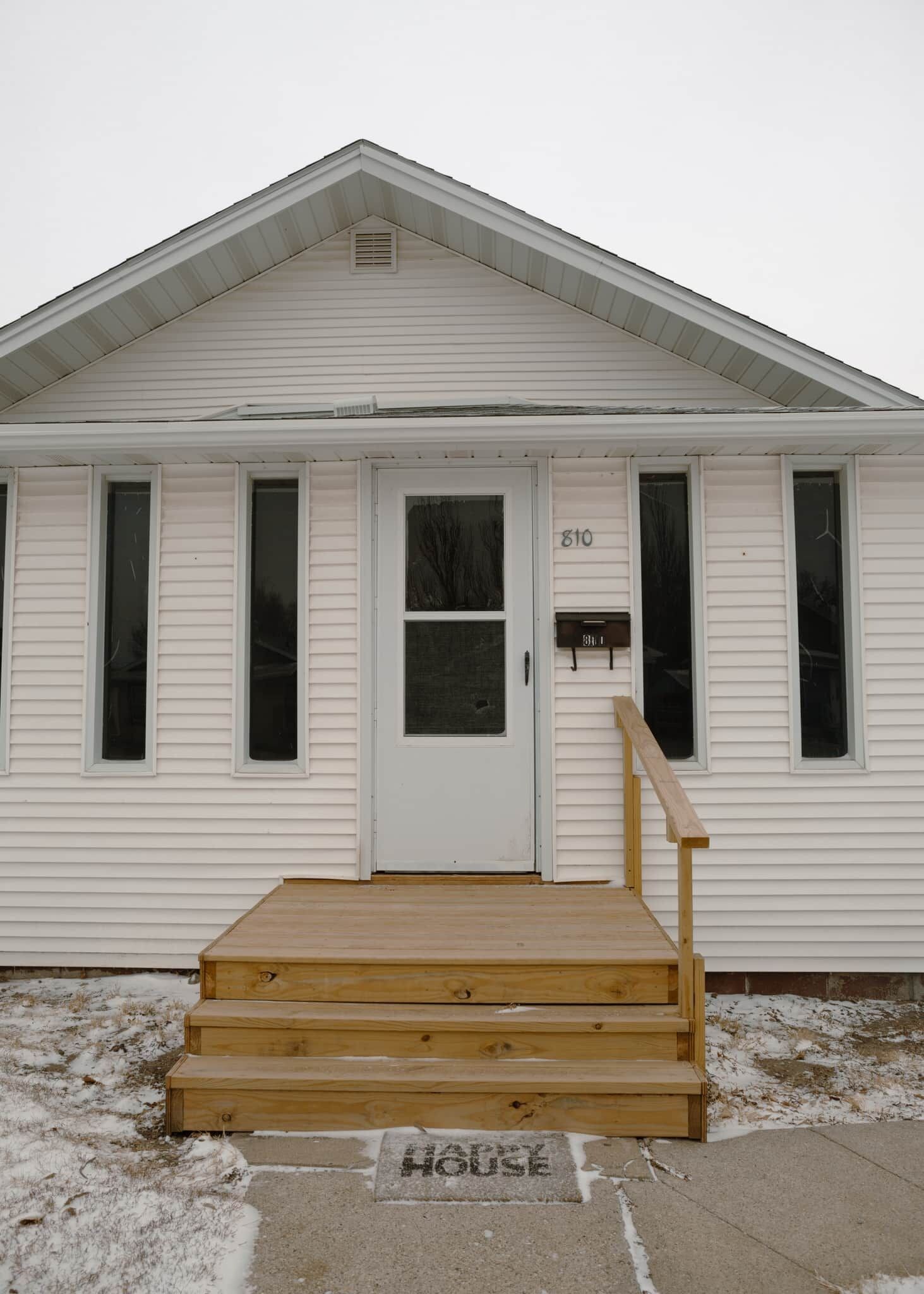 A single-story house with a front door, a small porch with steps, and a mailbox.