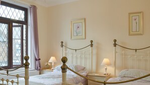 Un dormitorio con dos camas, una ventana con cortinas, mesitas de noche con lámparas y cuadros en la pared.