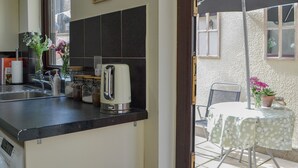 Una cocina con un tostador, un lavabo y una ventana. Hay una mesa con mantel afuera.