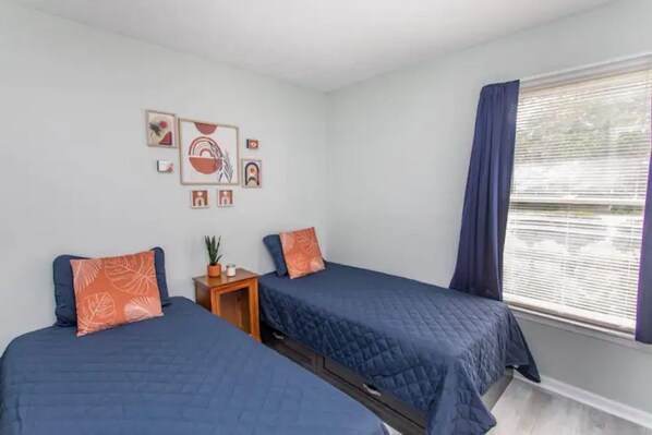 Un dormitorio con dos camas, una mesita de noche pequeña y una ventana con cortinas.