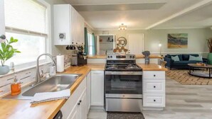A modern kitchen with white cabinets, a stainless steel stove, and a wooden countertop. - WinterBungalow (Myrtle Beach)