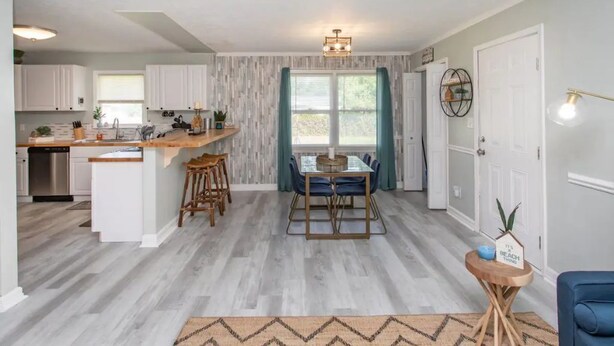 A modern kitchen with white cabinets, a wooden island, and a dining area with a glass table and blue chairs. - WinterBungalow (Myrtle Beach)