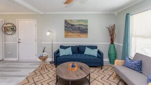 A living room with a blue sofa, a round coffee table, and a ceiling fan. - WinterBungalow (Myrtle Beach)