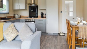 Eine kompakte Küche mit modernen Geräten, ein Essbereich mit Holzmöbeln und ein graues Sofa mit gemusterten Kissen.