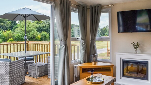 Ein Zimmer mit Holztisch, Korbstühle, Kamin und an der Wand montiertem Fernseher.