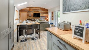 A modern kitchen with a wooden accent wall, a dining area with bar stools, and a welcoming sign.