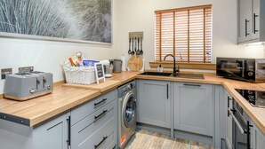 A modern kitchen with grey cabinets, a wooden countertop, a washing machine, and a large landscape painting.