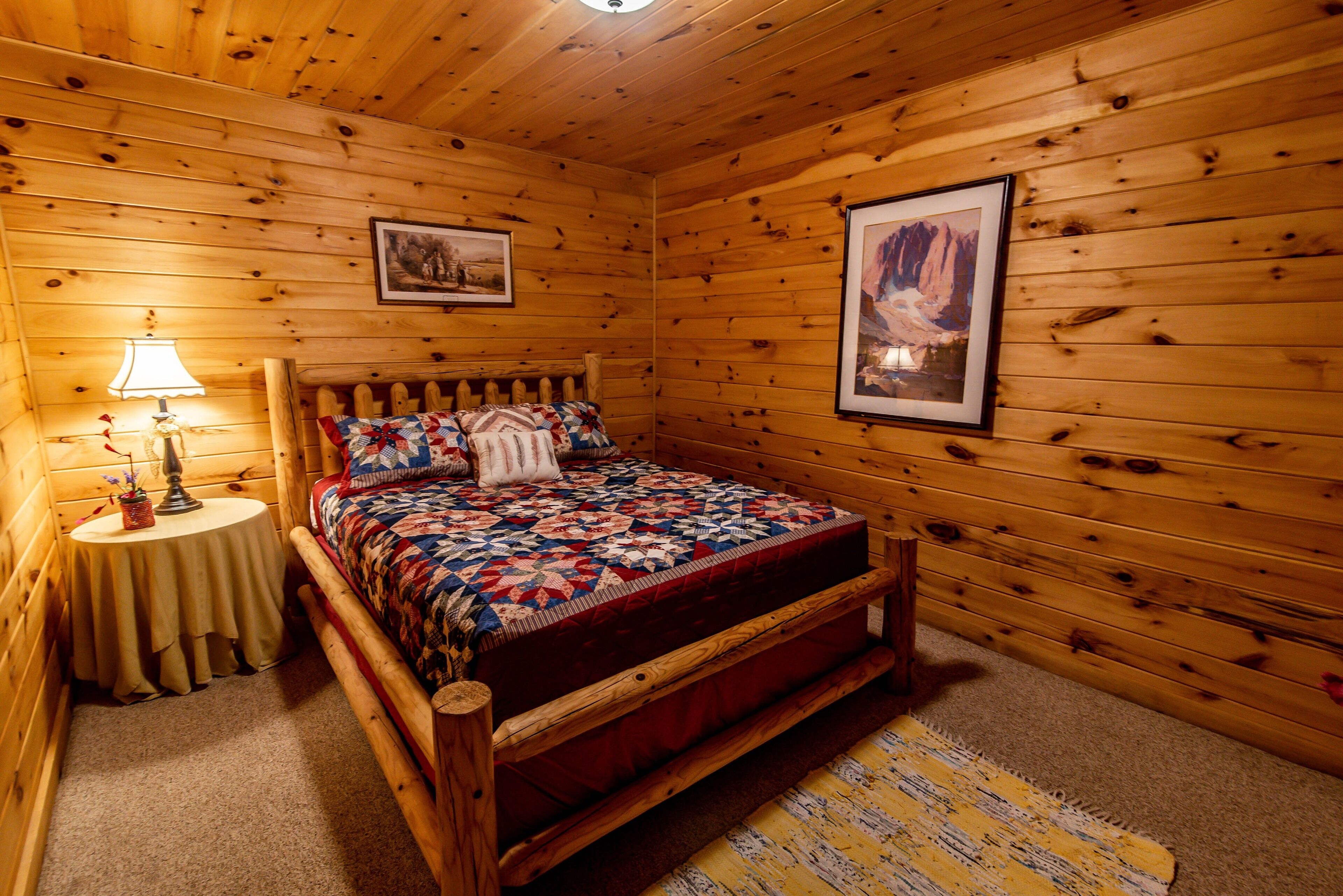 Ein Schlafzimmer einer Holzhütte mit einem Bett, einem Nachttisch, einer Lampe und zwei gerahmten Bildern an den Wänden.