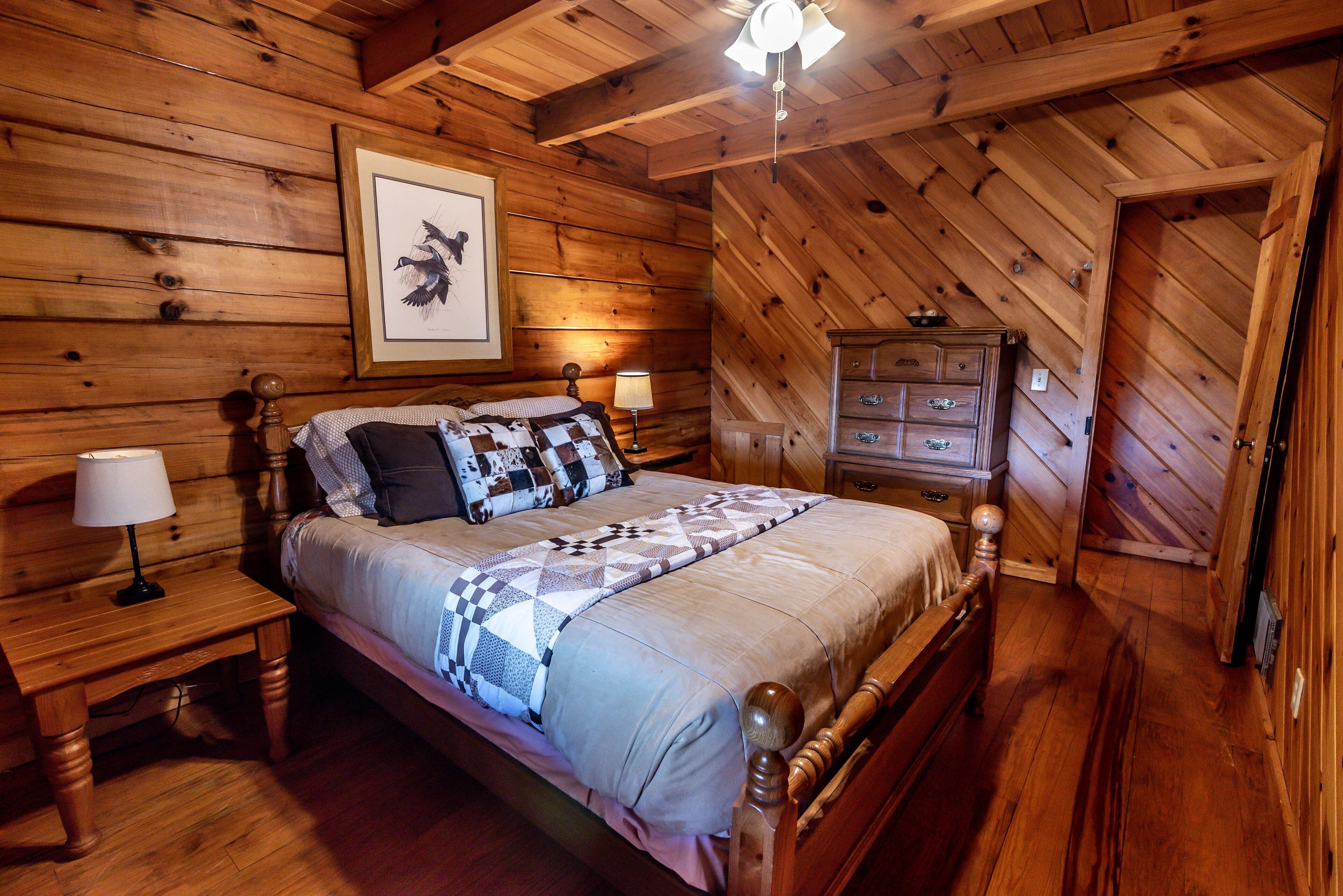 A wooden-paneled bedroom with a bed, nightstands, a dresser, and a ceiling fan.