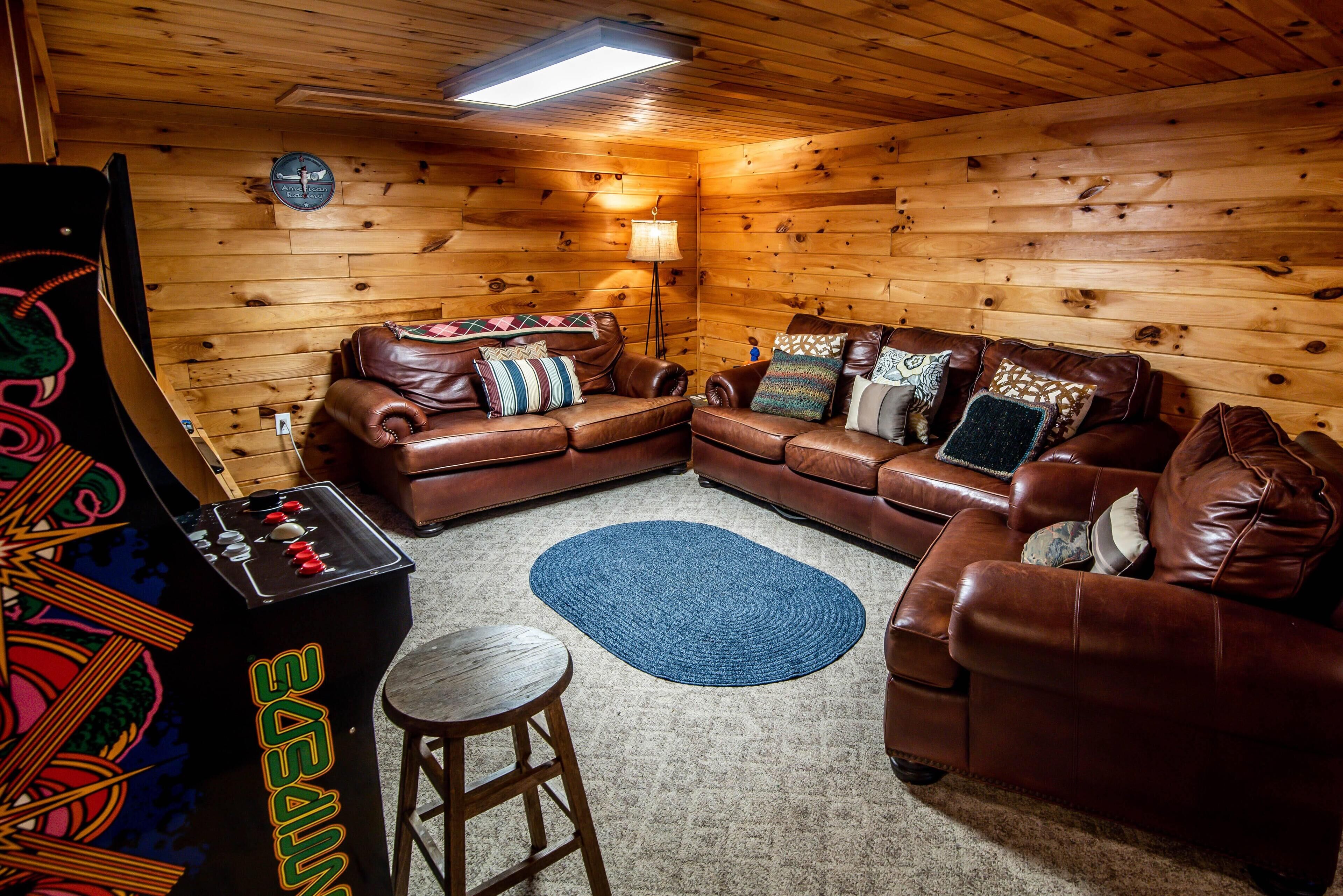 A cozy room with wooden walls, a brown leather sofa set, a blue rug, and a small wooden stool.