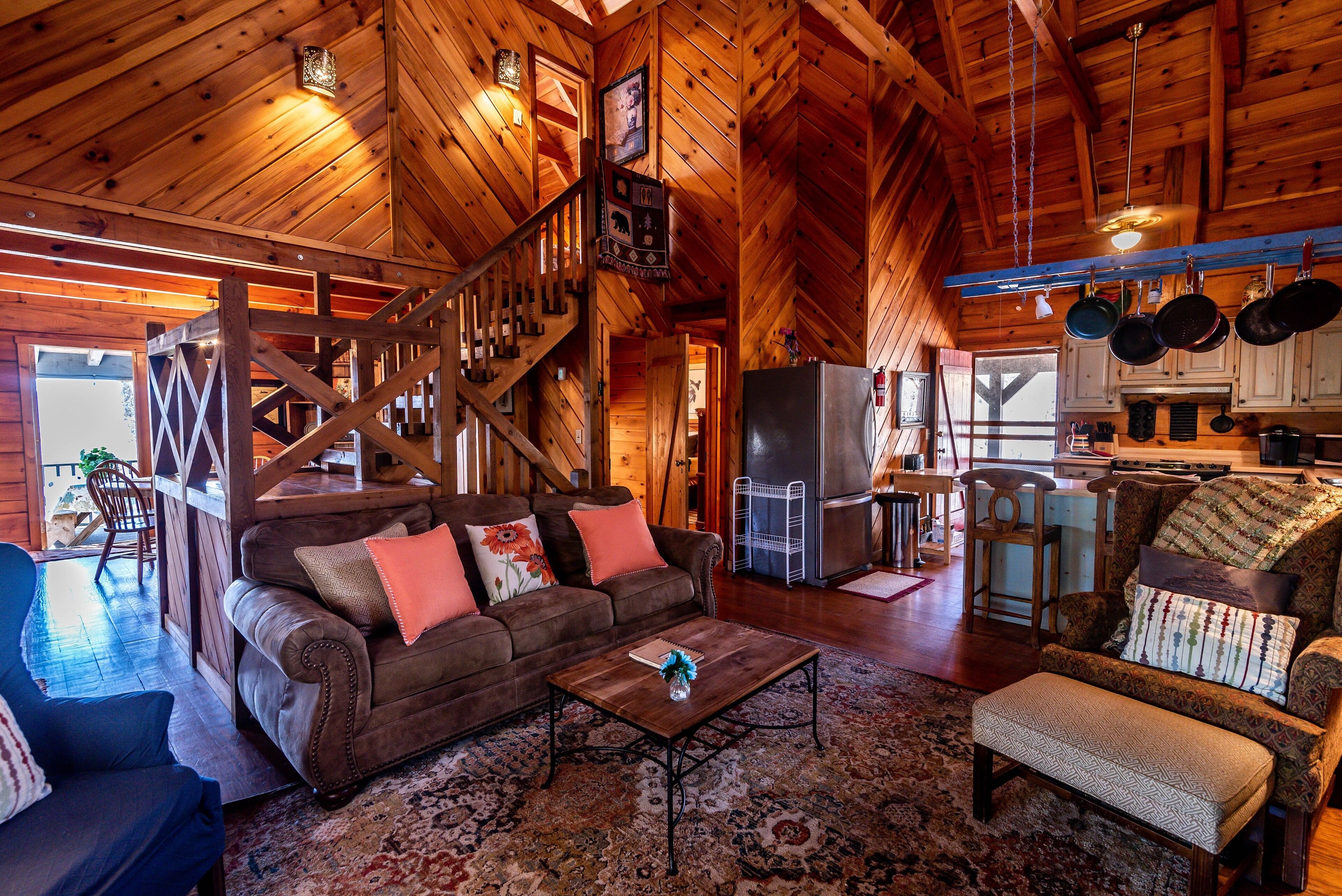 Een gezellig cabin interieur met een houten trap, een woonkamer met een bank en fauteuils, een eethoek en een keuken met hangende potten.