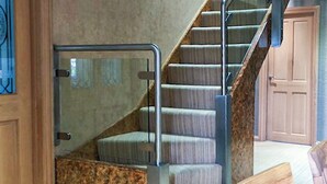 Un escalier doté d’une rampe métallique et de marches recouvertes de moquette, menant à une pièce avec une porte en bois et une fenêtre.