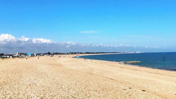 Une vaste plage de sable fin, sous un ciel bleu dégagé et une mer calme.