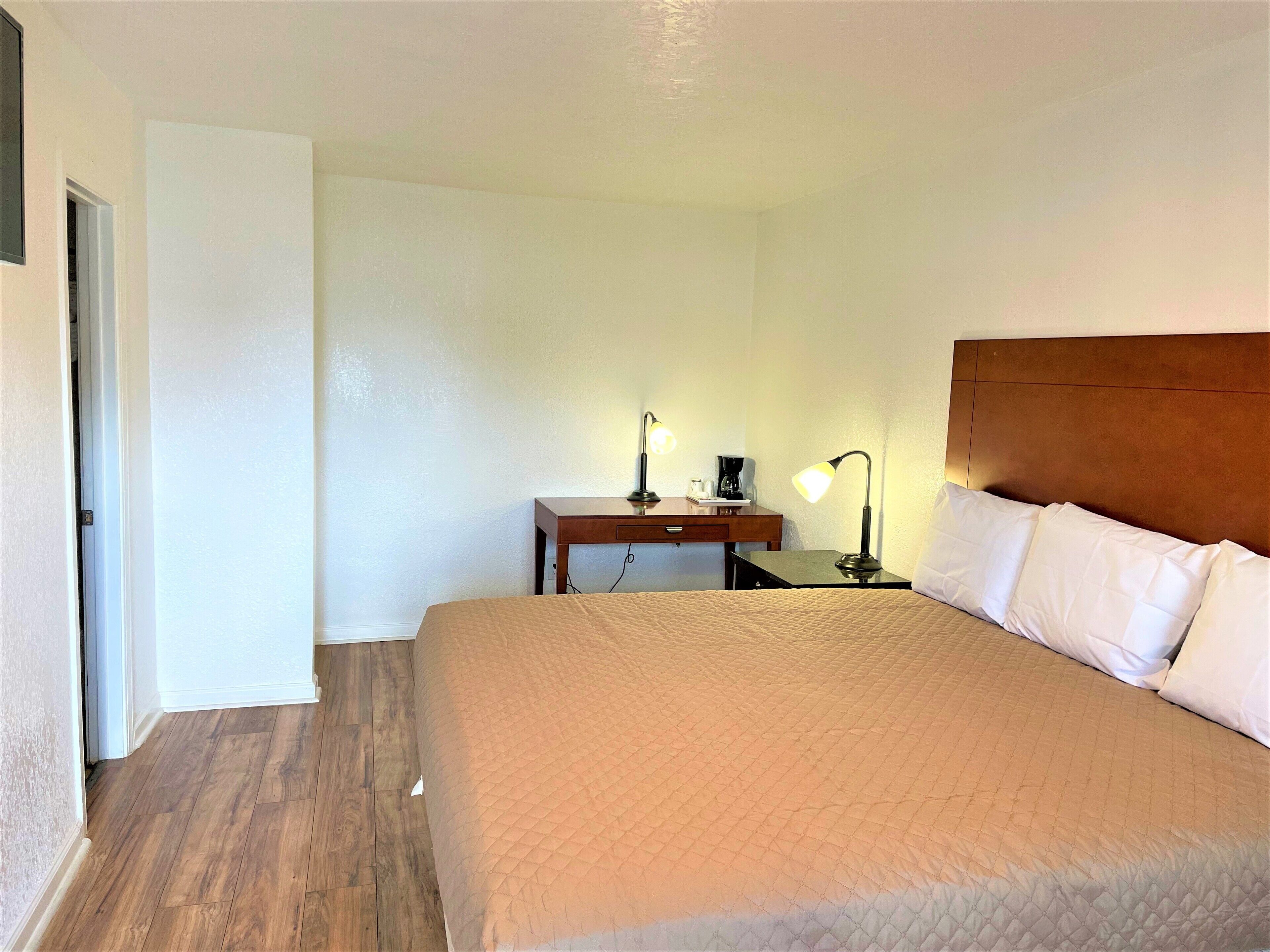 A hotel room with a bed, a desk, a chair, a lamp, and a coffee maker.