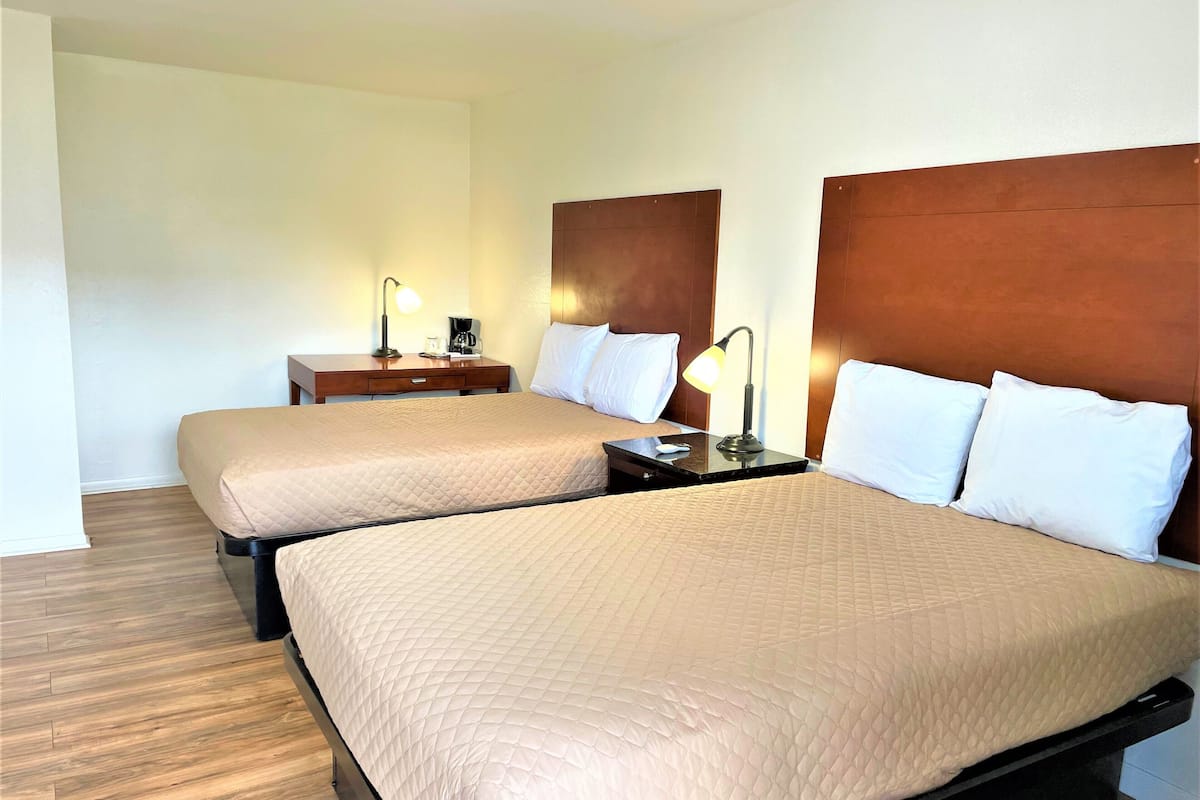 Habitación de hotel con dos camas, cabeceros de madera, mesitas de noche con lámparas y suelo de madera.