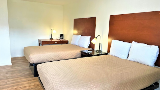 Habitación de hotel con dos camas, cabeceros de madera, mesitas de noche con lámparas y suelo de madera.